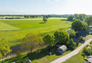 Vue aérienne d’une tiny house près d’une rivière et de champs verts au Holiday Park Mölke, Pays-Bas.