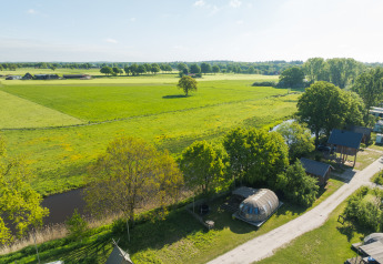 Vue aérienne d’une tiny house près d’une rivière et de champs verts au Holiday Park Mölke, Pays-Bas.