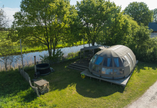 Luchtzicht op de Riverdome tiny house met badkamer en hot tub bij Holiday Park Mölke, Nederland, aan de rivier.