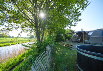 Vue ensoleillée au bord de la rivière avec Riverdome, terrasse en bois, table et bain chaud à Holiday Park Mölke.