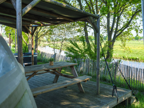 Outdoor seating with covered wooden picnic bench by a river, Riverdome tiny house at Holiday Park Mölke, NL.