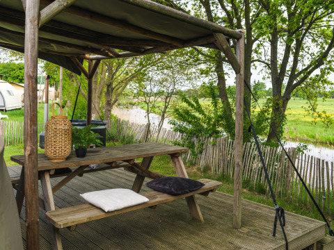 Udendørs siddeområde med træbord, puder og lanterne, udsigt til grønne marker ved Holiday Park Mölke.