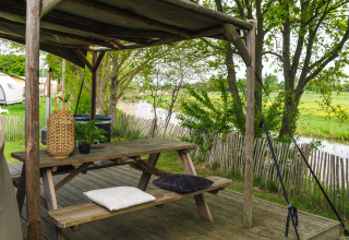Buiten zitgedeelte met houten picknicktafel, kussens en lantaarn, uitzicht op velden bij Mölke.