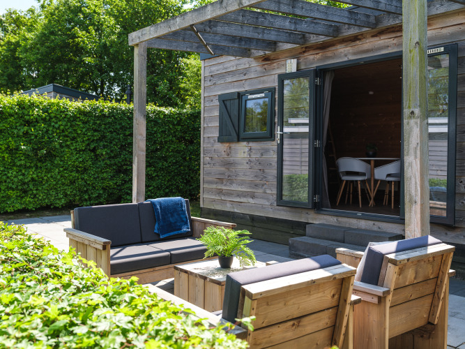 Buiten zithoek met houten meubels bij Tiny House in Holiday Park Mölke, omgeven door groen.