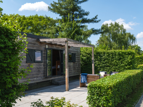 Gemütliches Tiny House aus Holz mit Terrasse und grüner Hecke im Holiday Park Mölke, Niederlande.