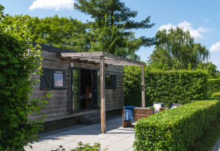Wooden tiny house with open patio area and lush hedges at Holiday Park Mölke in the Netherlands.