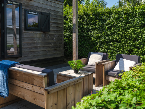Gemütliche Terrasse am Tiny House im Holiday Park Mölke, Niederlande, mit Holzsitzmöbeln und Pflanzen.