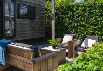 Buitenterras van Tiny House bij Holiday Park Mölke in Nederland met houten meubelen en groene haag.