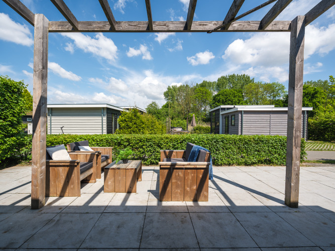 Terras met houten zitmeubilair bij Tiny House in Holiday Park Mölke, Nederland, onder een pergola.