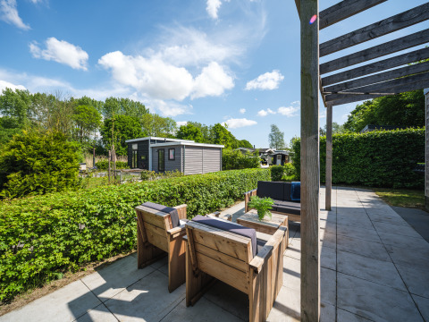 Sonnige Terrasse beim Tiny House im Holiday Park Mölke, Niederlande, mit Holzmöbeln und grüner Hecke.