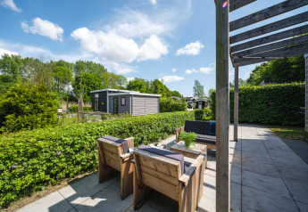Sonnige Terrasse beim Tiny House im Holiday Park Mölke, Niederlande, mit Holzmöbeln und grüner Hecke.