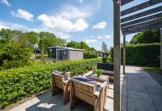 Outdoor patio at Tiny House in Holiday Park Mölke, Netherlands, with wooden seating and lush green hedges.