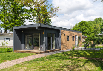 Moderne tiny cabin bij Holiday Park Mölke in Nederland, omringd door bomen en verzorgd gazon.