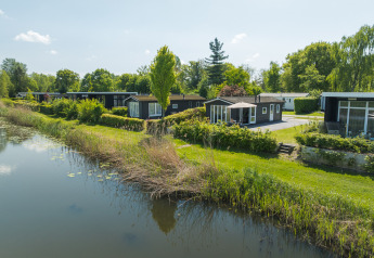 Bungalow ved Regge, Holiday Park Mölke, Nederlandene, ved en sø omgivet af natur og grønne områder.