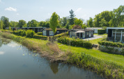 Bungalow ved Regge, Holiday Park Mölke, Nederlandene, ved en sø omgivet af natur og grønne områder.