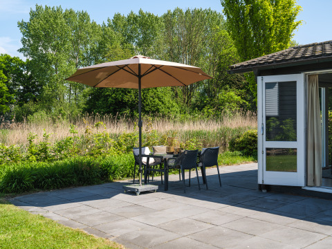Terras van Bungalow at the Regge in Holiday Park Mölke met parasol, stoelen en veel groen.