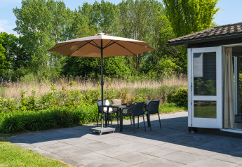 Terras van Bungalow at the Regge in Holiday Park Mölke met parasol, stoelen en veel groen.