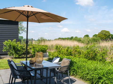 Outdoor dining area with umbrella and field view at Bungalow at the Regge, Holiday Park Mölke, Netherlands.