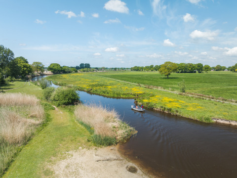 Zicht op rivier en boot bij Bungalow at the Regge, Holiday Park Mölke, Nederland, groene weiden onder blauwe lucht.