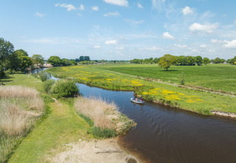 Vue sur la rivière avec bateau près du Bungalow at the Regge, Holiday Park Mölke, Pays-Bas, champs et ciel bleu.