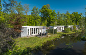 Lodge Mistique ved Holiday Park De Lochemse Berg, Holland, ved en kanal, omgivet af grønne træer.