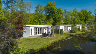Lodge Mistique at Holiday Park De Lochemse Berg, Netherlands, modern lodges by a canal and green trees.