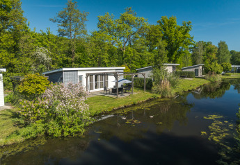 Lodge Mistique at Holiday Park De Lochemse Berg, Netherlands, lakeside with lush green trees in summer.