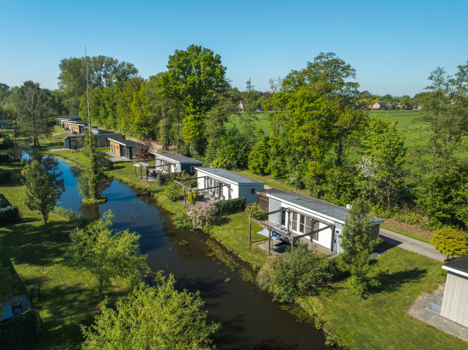 Luftfoto af Lodge Mistique ved Holiday Park De Lochemse Berg i Holland, omgivet af grønt og en kanal.