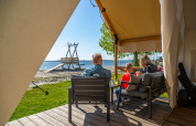 Family relaxing on a safari tent porch by the beach at Zuiderzee, Netherlands, enjoying the sunny weather.