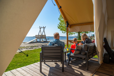 Famiglia che si rilassa sulla veranda di una tenda safari fronte spiaggia a Zuiderzee, Paesi Bassi, al sole.