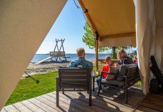 Famiglia che si rilassa sulla veranda di una tenda safari fronte spiaggia a Zuiderzee, Paesi Bassi, al sole.