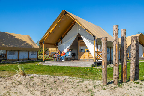 Family enjoying the outdoors on a porch of a Glampingtent Beachfront Luxe with a bright blue sky above.