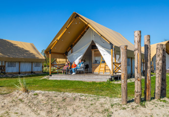 Familie sidder foran en luksuriøs Glampingtent Beachfront Luxe under blå himmel og nyder campinglivet.