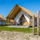 Familie sidder foran en luksuriøs Glampingtent Beachfront Luxe under blå himmel og nyder campinglivet.