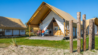 Familie entspannt vor einem luxuriösen Glampingtent Beachfront Luxe unter klarem Himmel beim Camping.