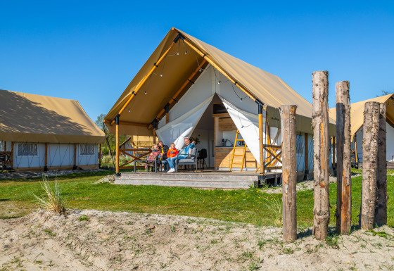 Famiglia rilassata davanti alla Glampingtent Beachfront Luxe sotto un cielo blu, godendo la vacanza.