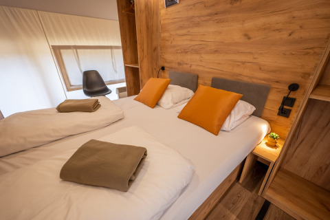 Indretning af soveværelse i Glampingtent Beachfront Luxe på Zuiderzee, Holland, med dobbeltseng og træpaneler.