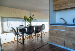 Interno del Glampingtent Beachfront Luxe a Zuiderzee, Paesi Bassi, tavolo da pranzo, cucina e fiori.