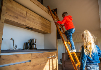 Two children exploring a loft area with a ladder in a modern kitchen of a beachfront glamping tent in Netherlands.