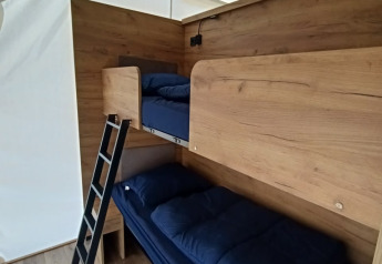 Binnenzicht van Glampingtent Beachfront Luxe aan Zuiderzee met stapelbedden en donkerblauw beddengoed.