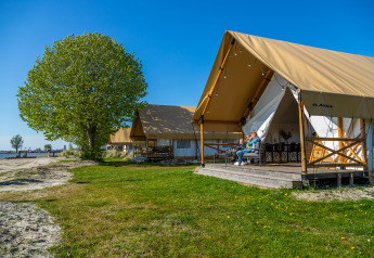 Safari-Zelt am Wasser im Zuiderzee, Niederlande, mit entspannter Familie auf der Terrasse unter blauem Himmel.
