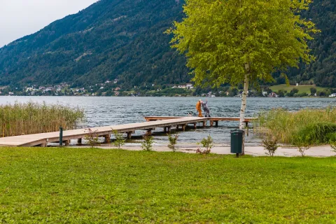 Udsigt over søen ved Cottage Hot tub på Ossiacher See i Østrig med en mole, træ og bjerge.