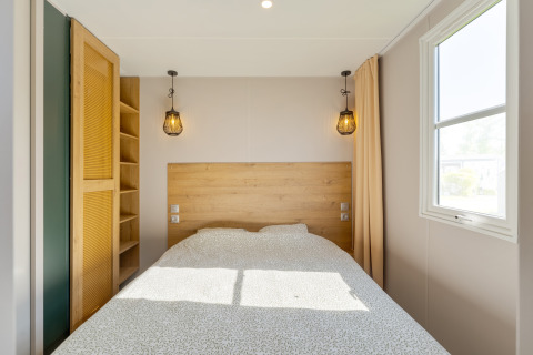 Slaapkamer in Vakantiehuis Familie op Camping Papillon met dubbel bed, raam en sfeervolle verlichting.