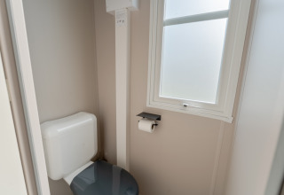 Lichte wc met toilet, toiletrolhouder en raam in Vakantiehuis Familie (PL.82) bij Camping Papillon.