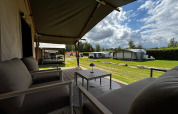 Vue depuis la terrasse d'une tente safari avec fauteuils et table, entourée de verdure et d'autres tentes.