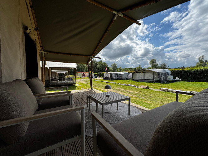 Blick von einer Safari-Zeltterrasse mit gemütlichen Sitzgelegenheiten, anderen Zelten und grünem Rasen.