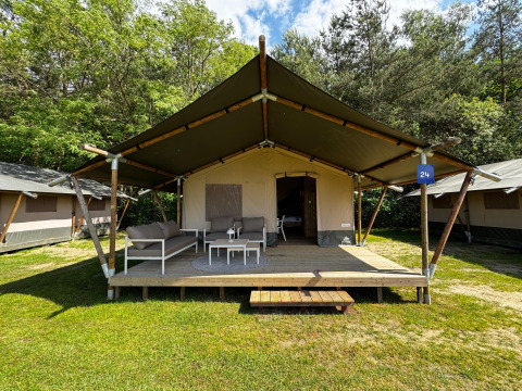 Tienda safari en un camping con porche cubierto, asientos exteriores y entorno natural verde.
