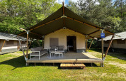 Tente safari sur un camping avec terrasse couverte, mobilier extérieur et verdure environnante.