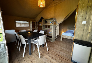 Intérieur d'une tente safari avec plancher en bois, table à manger, chaises, frigo et lits.