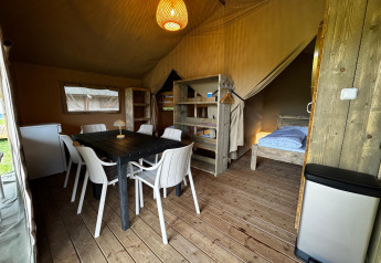 Intérieur d'une tente safari avec plancher en bois, table à manger, chaises, frigo et lits.